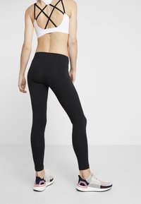 Czarne legginsy o dopasowanym kroju, w parze z białym stroj sportowym z krzyżowym tyłem. Sneakersy mają przewiewną siateczkową cholewkę i amortyzującą podeszwę.