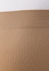 Leggings beige côtelés avec une large ceinture. Texture légère avec un léger éclat, présentant des côtes horizontales sur tout le tissu.