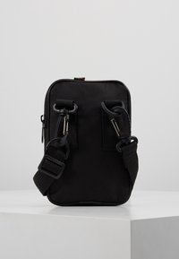 Mustassa kankaisessa olkalaukussa on kaksi tukevää klipsiä, säädettävä hihna ja vetoketjutasku. Laukku on muotoiltu yksinkertaiseksi suorakulmioksi.