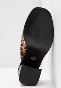 Chaussure à talons hauts en imprimé léopard avec une semelle synthétique noire, présentant une surface lisse et un design à bout rond.