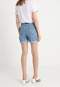 Světle modré denimové kraťasy s ohrnutými manžetami, vysokým pasem a dvěma zadními kapsami. Oblékané s světle fialovou košilí s krátkým rukávem a bílými sandály na podpatku.