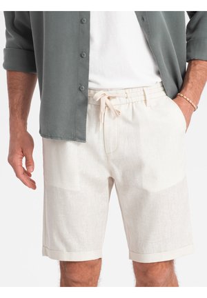 Shorts beige clair avec une taille élastique et un cordon de serrage, dotés d'une finition texturée et d'un ourlet replié. Portés avec une chemise grise à boutons.