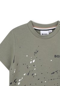 T-shirt verde oliva a maniche corte con collo rotondo, caratterizzato da motivi di schizzi neri e bianchi e un logo "BOSS" in stampa scura.