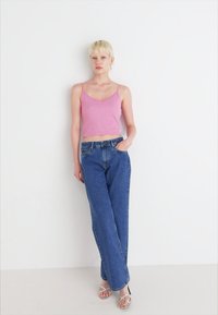 Roosa lühike tank top spagetirihmadega, koos kõrge talje ja vaba lõikega siniste denimitehindadega ning hõbedaste rihmadega sandaalidega.