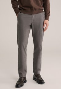 Szürke, finom mintás, egyenes szabású szabott nadrág két oldalzsebbel, sötétbarna mokaszinokkal párosítva. Az anyag könnyűnek tűnik.