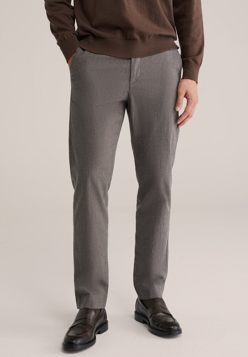 Szürke, finom mintás, egyenes szabású szabott nadrág két oldalzsebbel, sötétbarna mokaszinokkal párosítva. Az anyag könnyűnek tűnik.