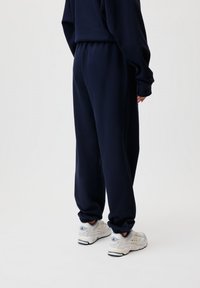 Marineblaue Jogginghosen mit einem elastischen Bund, schmal zulaufenden Beinen und weichem Material. Getragen mit weißen Sportschuhen mit grauen Akzenten.