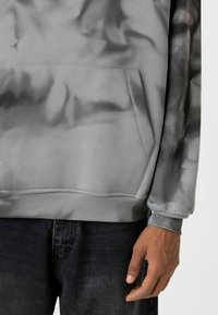 Grijze hoodie met een zachte, gestructureerde stof, een voorzak en een iets ontspannen pasvorm. De mouw heeft een zwart verloopontwerp.