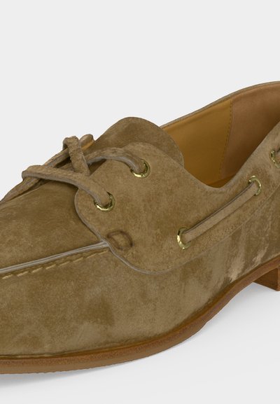 Ταμπά μοκασίνι από σουέντ δέρμα με δέσιμο μπροστά, χρυσά μεταλλικά, ραφές μοκασίνου και καφέ καουτσούκ σόλα.