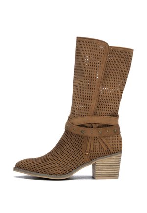 Bota marrón de ante perforada hasta la mitad de la pantorrilla con correa decorativa y tachuelas metálicas, puntera puntiaguda y tacón de bloque apilado sobre fondo blanco.