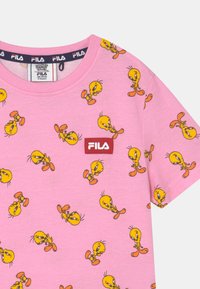 T-shirt de algodão cor-de-rosa com um padrão repetido de personagens Tweety Bird amarelos. Logótipo da Fila em vermelho bordado na frente. Mangas curtas.