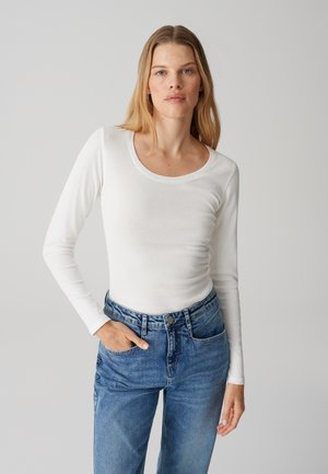 Witte lange mouw top met een ronde halslijn, gecombineerd met hoge taille blauwe jeans. De stof lijkt soepel en licht getailleerd te zijn.