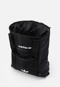Svart Adidas toteväska med dubbla handtag, framficka med dragkedja och vit Adidas-logotyp på enfärgad bakgrund.