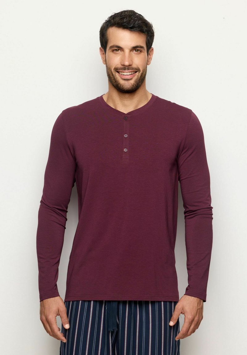 Burgundy långärmad henleytröja med rund halsringning och tre knappar fram. Mjuk textur och figurnära design.