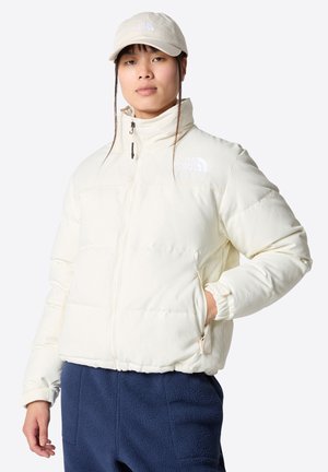 Witte pufferjack met hoge kraag, ritssluiting aan de voorkant en elastische manchetten. Voorzien van logo op de borst. Draagt bij navy fleece broek.