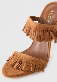 Brown suede high-heeled sandal featuring two fringe-accented straps and a smooth leather insole, with a pointed toe design.