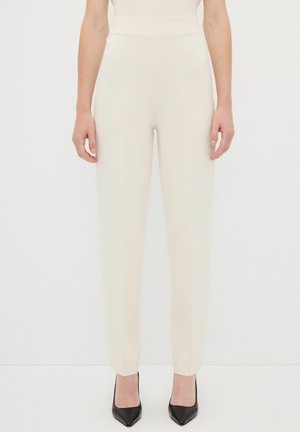 Cream-colored tailored pants with a high waist, tapered shape, and visible stitching. Paired with black high-heeled shoes.