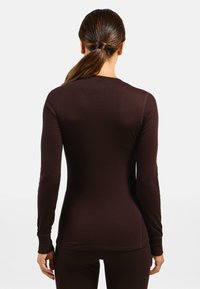 Brown long-sleeve top made of ribbed fabric, featuring fitted design, rounded neckline, and stitched seams on sleeves and hem.