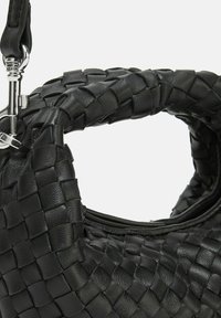 Sac à main en cuir noir avec une texture tissée, doté d'une poignée arrondie et de accents en métal argenté. Fermeture éclair en haut.
