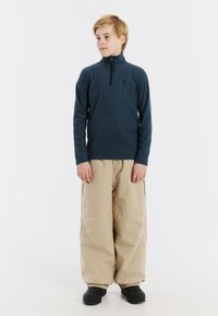 Pullover in pile blu navy con colletto alto e zip frontale, abbinato a pantaloni cargo beige oversize e calzature nere.
