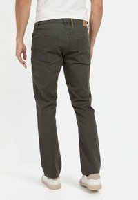 Dunkelgrüne Baumwollhose mit gerader Beinform, Gesäßtaschen und einem Lederlabel am Bund. Kombiniert mit weißen Sneakers.