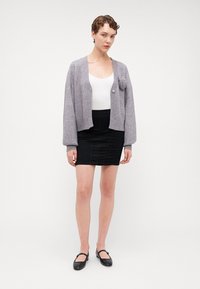 Harmaa neulottu neuletakki, jossa on tasku, yhdistettynä hyvin istuvaan mustaan hameeseen ja mustiin tasapohjaisiin kenkiin. Yksinkertainen muotoilu, jossa napitus ja resorit.