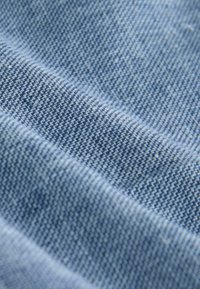 Tejido de mezclilla azul con un tejido texturizado, que presenta hilos claros y oscuros alternados en un patrón espina de pescado. Suave al tacto.