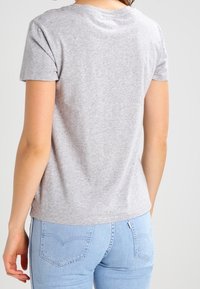 Grå kortærmet t-shirt i blødt stof, med rund halsudskæring og let buet kant, parret med lyseblå jeans.