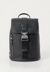 Svart skinnryggsekk med klaff og sølvfarget metallspenne. Har sidelomme med glidelås, teksturert overflate, og merkevarestropp. Formen er rektangulær.