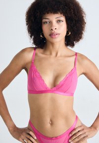 Vaaleanpunainen alusvaatesetti, jossa on läpinäkyvä bralette, jossa on pitsireunus, ja yhteensopivat korkeat alushousut. Sujuva pinta ja hienovaraiset yksityiskohdat.