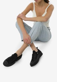 Sorte sneakers med rund toet, tekstureret overflade og gummisål. Bæret med lyseblå jeans med frynset kant og afslappet pasform.