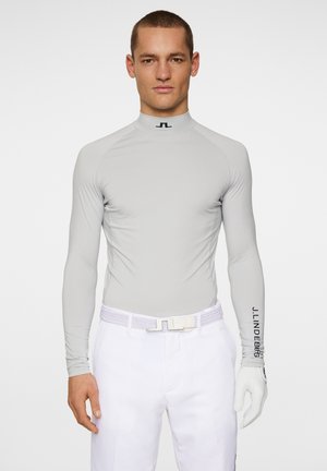 Light gray long-sleeve performance shirt with a high collar. Features J.Lindberg logo on the right sleeve, fitted design, and smooth texture.