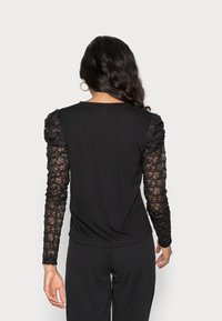 Top preto com mangas de renda em padrão floral, decote redondo e um corte descontraído. As costas têm um tecido liso sem detalhes.