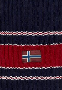 Mørkeblå og rød strikketrøje med hvide og røde striber, prydet med et rektangulært lædermærke, der viser det norske flag.
