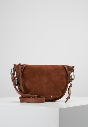 Sac bandoulière en daim marron avec sangle en cuir réglable, ferrures argentées et fermeture éclair, posé sur une surface blanche sur fond gris.