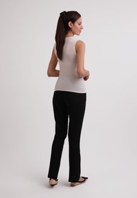 Weißes ärmelloses Oberteil kombiniert mit schwarzen, figurbetonten Hosen und flachen Schuhen, die eine glatte Textur und ein einfaches Design aus seitlicher und Rückansicht zeigen.