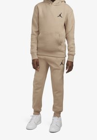 Sudadera beige de Jordan y pantalones de chándal a juego, con acentos de logo en negro. Tejido suave con un corte relajado y detalle de bolsillo canguro.