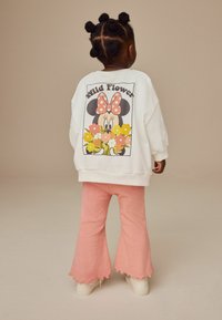 Vit sweatshirts med "Minnie Mouse" grafik, prydd med blommor och prickar. Matchad med ribbade, utsvängda rosa byxor och vita skor.