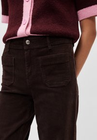 Καφέ παντελόνι κοτλέ με ψηλή μέση, που διαθέτει δύο πίσω τσέπες και κλείσιμο με μεταλλικό κουμπί, σε συνδυασμό με πουλόβε�ρ πλεκτό σε μπουρντό και ροζ χρώμα.