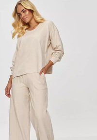 Beżowy, oversize'owy sweatshirt z opadającymi ramionami i ściągaczami, w komplecie z dopasowanymi, szerokimi spodniami z miękkiego materiału.