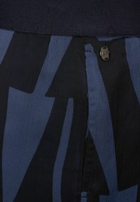 Niebieska i czarna tkanina w wzory z teksturowanym pasem; posiada mały metalowy guzik oraz widoczne detale szwów.