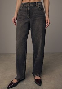 Jeans de pierna recta de lavado oscuro, hechos de mezclilla, que presentan un diseño clásico de bolsillo delantero, costuras amarillas en contraste y una cinturilla alta.