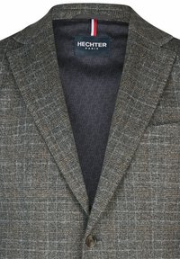 Grau kariertes Blazer mit strukturiertem Design, Reverskragen, brauner Naht und navyfarbener gemusterter Fütterung. Knopfdetail sichtbar.