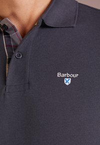Polo shirt marine foncé en tissu texturé avec un col. Doté d'un sous-col à carreaux et d'un logo brodé sur la poitrine.