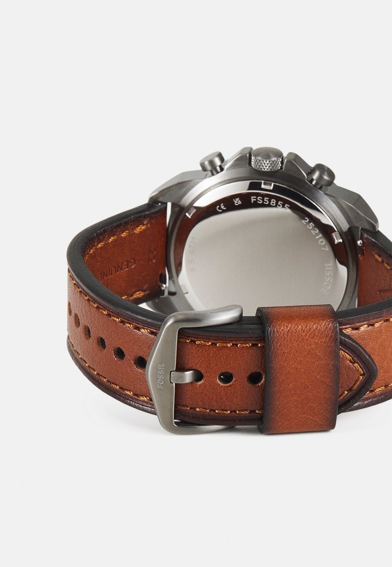 Bracelet de montre en cuir brun avec une boucle en acier inoxydable, couture détaillée et perforations pour réglage. Boîtier rond et surface polie.