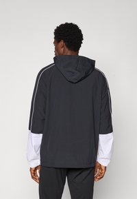 Sort og hvid hættejakke med lange ærmer, elastiske manchetter og hvide sidedele. Letvægtsmateriale med en afslappet pasform.