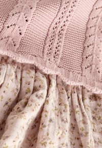 Tissu tricoté doux rose avec des motifs complexes superposé sur un tissu léger à motifs floraux froncés aux tons verts et violets atténués.