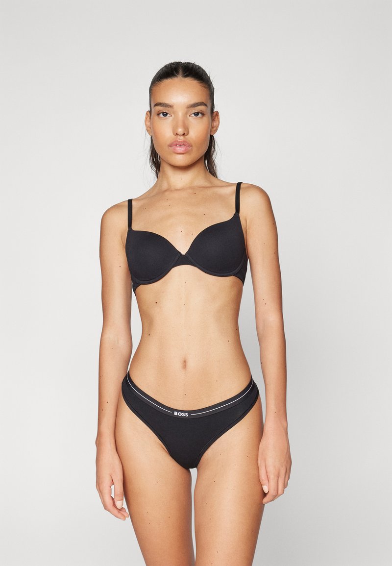 Soutien-gorge noir avec coques rembourrées et fines bretelles, associé à un string noir assorti avec une bande logo et un design épuré et minimaliste.
