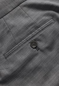 Tissu gris texturé avec un motif en chevrons, comprenant une poche passepoilée et une fermeture à bouton noir unique.