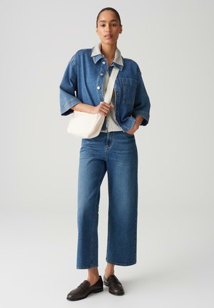 Blaues Denim-Übergröße-Jacke, gestreiftes Hemd, weit geschnittene blaue Jeans und dunkle Loafers, mit einer cremefarbenen Umhängetasche. Glatte Stoffstruktur.